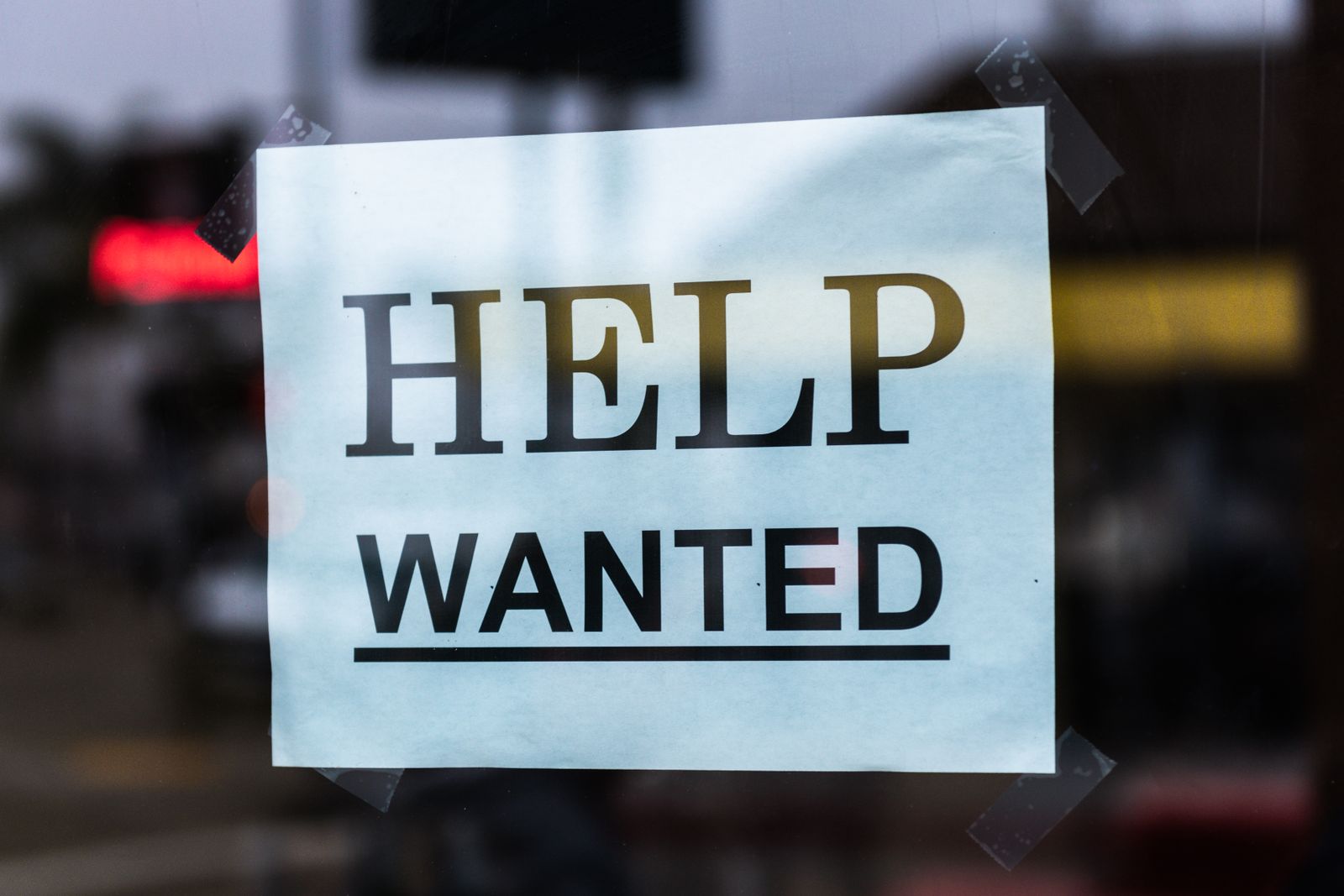 A 'Help Wanted' sign taped to a storefront window, representing U.S. job openings data
